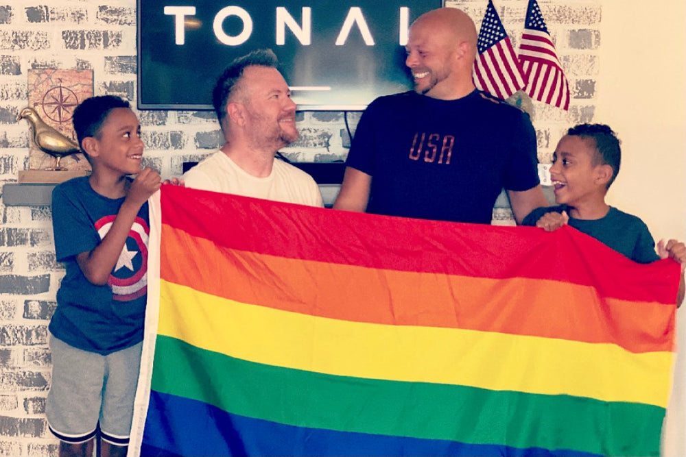 two men hold up the Pride flag with their twin sons