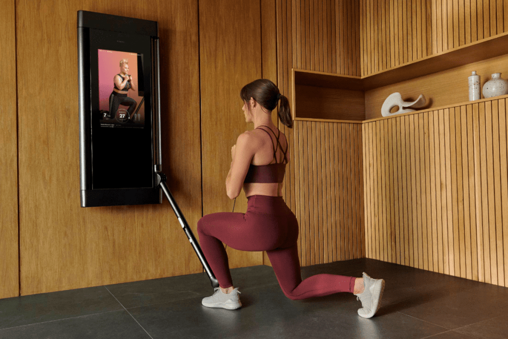 A woman is working out in her home, using Tonal to complete a goblet reverse lunge.