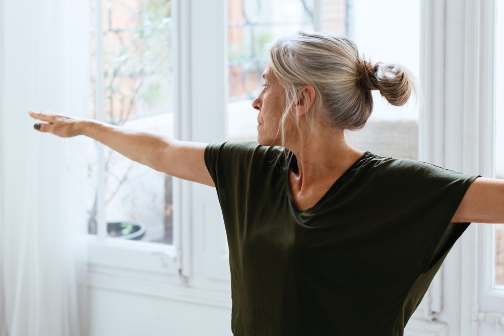 a woman with grey hair and a t-shirt doing the warrior yoga pose