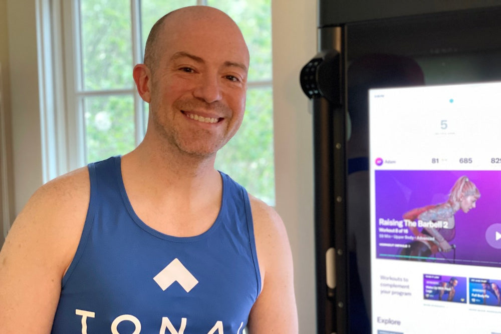 a man smiling in front of his tonal in a blue workout vest that say tonal