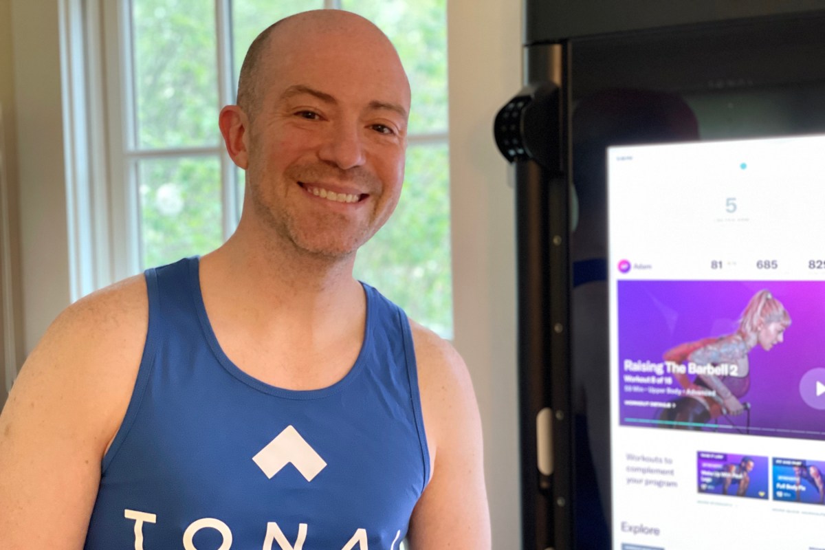 a man smiling in front of his tonal in a blue workout vest that say tonal