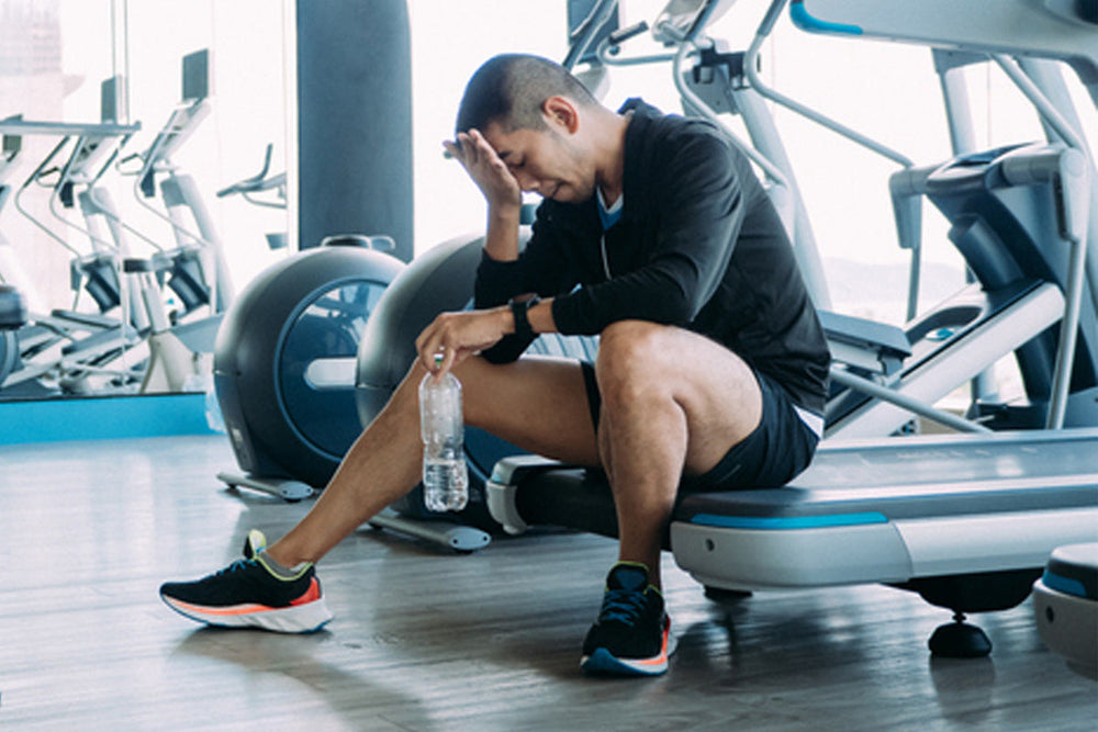Man sitting on treadmill with palm to his forehead.