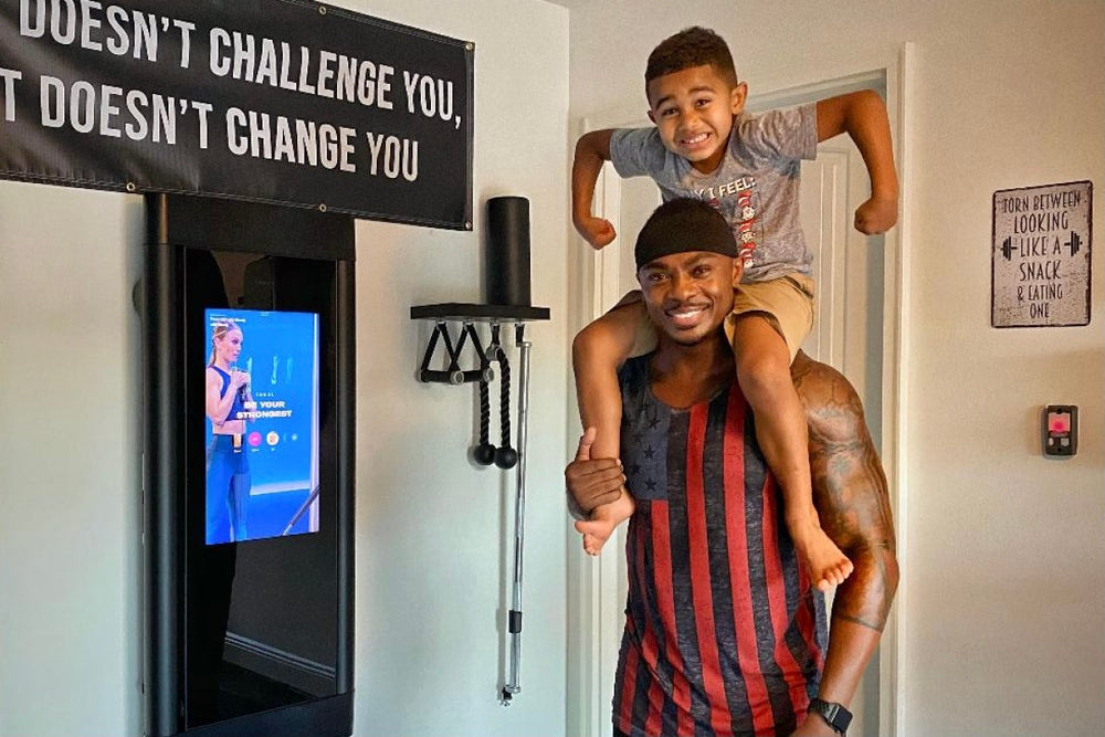 James Morgan smiles in front of his Tonal with his son on this shoulders