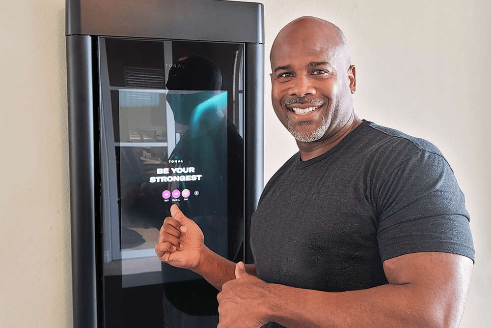 a man smiling and standing in front of his Tonal with his thumbs up