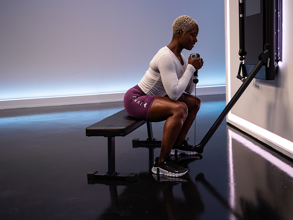 Tonal instructor seated on bench lifting Tonal smart handle

