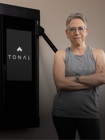 A lady posing next to a Tonal weight training system mounted to a wall