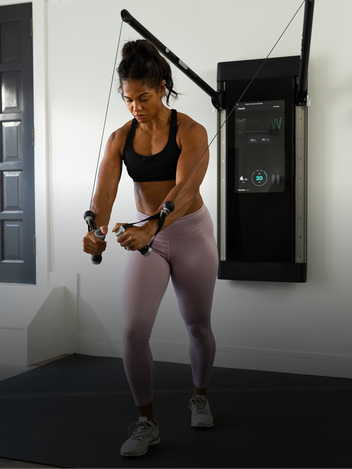 Woman exercising using a Tonal weight training system like a cable machine in a home gym setting