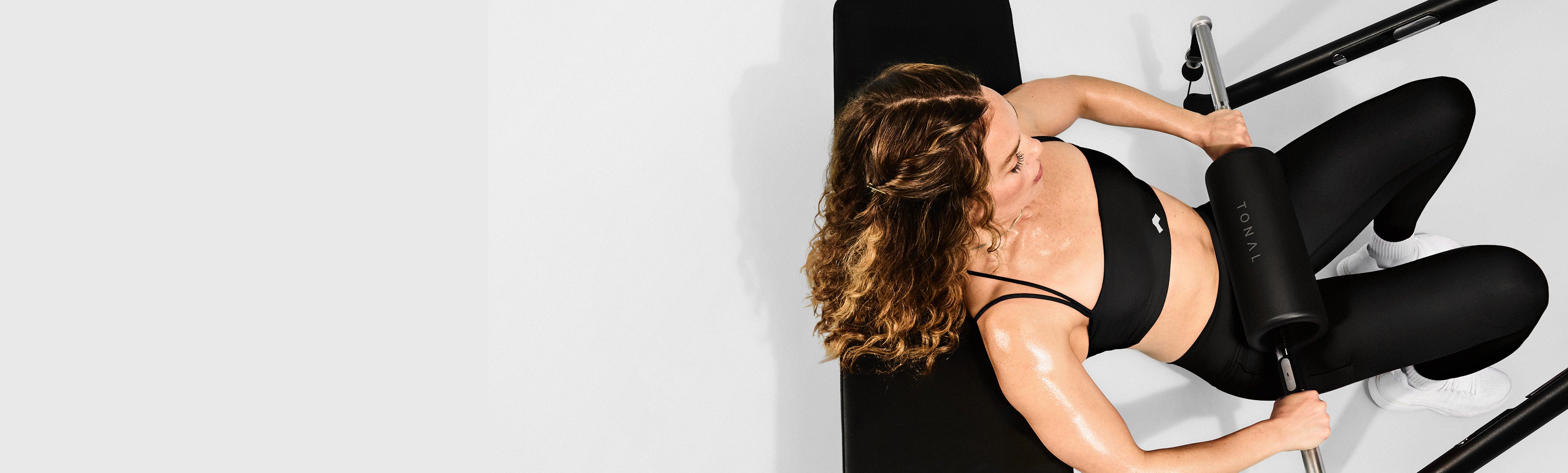 Woman performing a hip thrust using a wall-mounted exercise machine, Tonal.