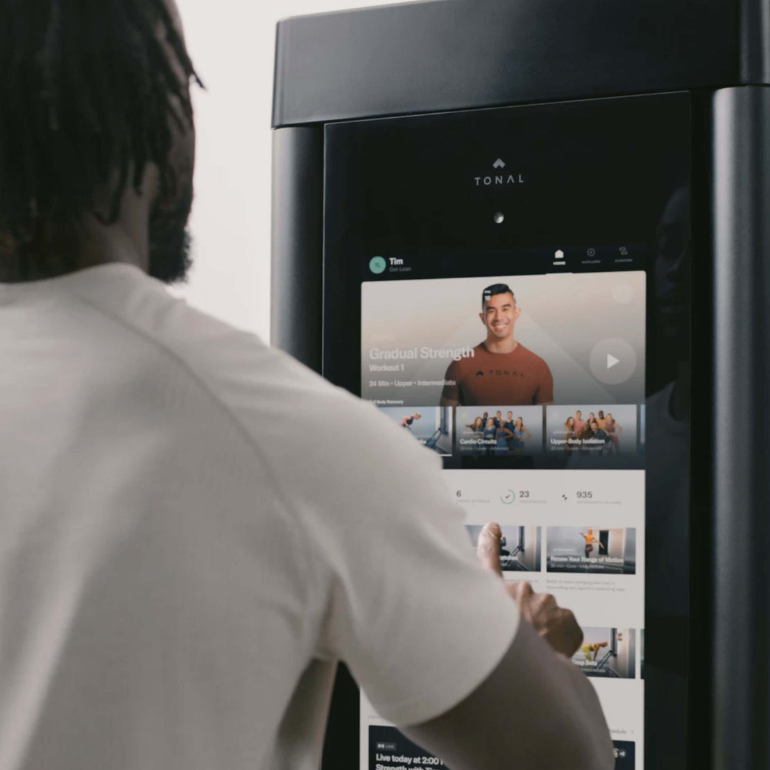 Person interacting with a Tonal fitness device displaying an app interface.