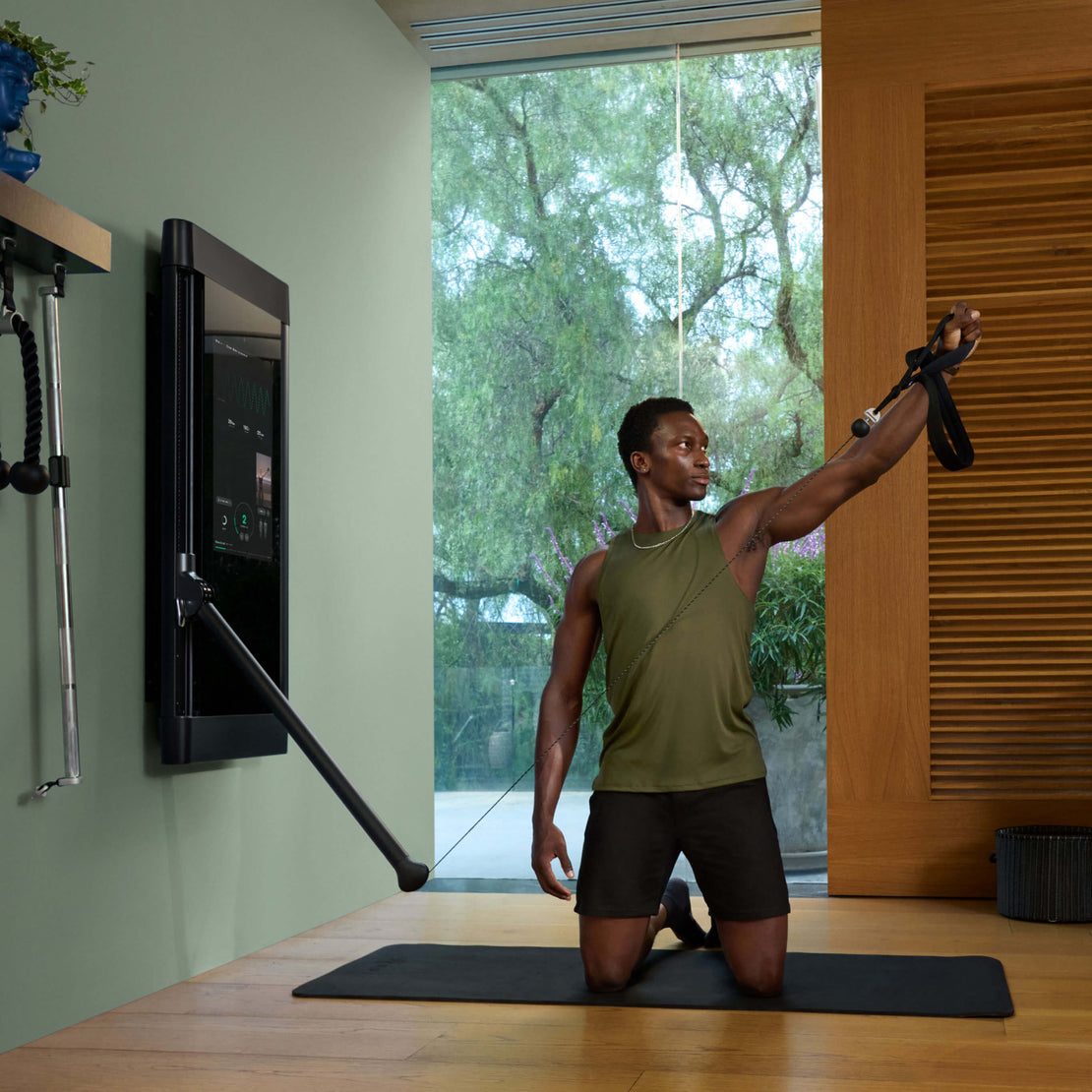 Man performing Pilates with Tonal Pilates Straps on Tonal 2 in a room with large windows showing greenery outside.