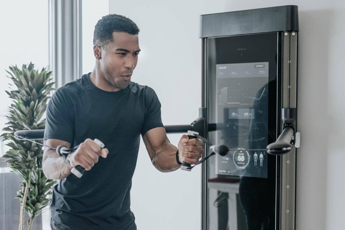 a smily man using a tonal — a slim flatscreen-like exercise machine that sits on the wall