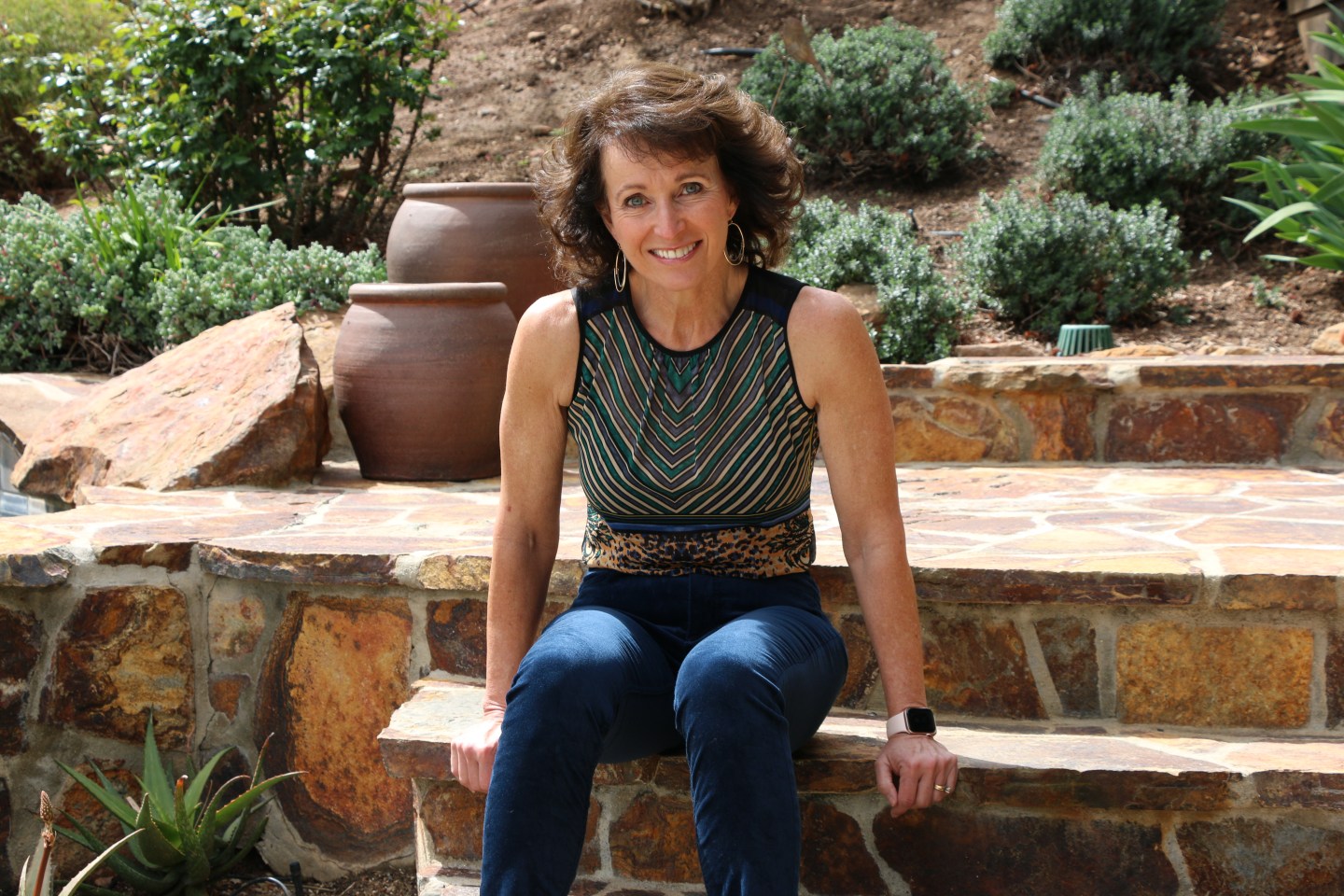 a woman sits on a set of stone steps outside and looks into the camera smiling