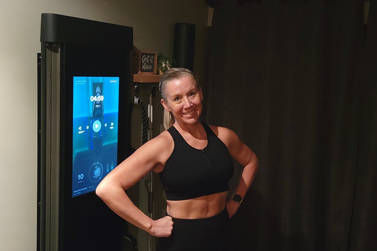 A woman in front of her Tonal exercise machine smiling