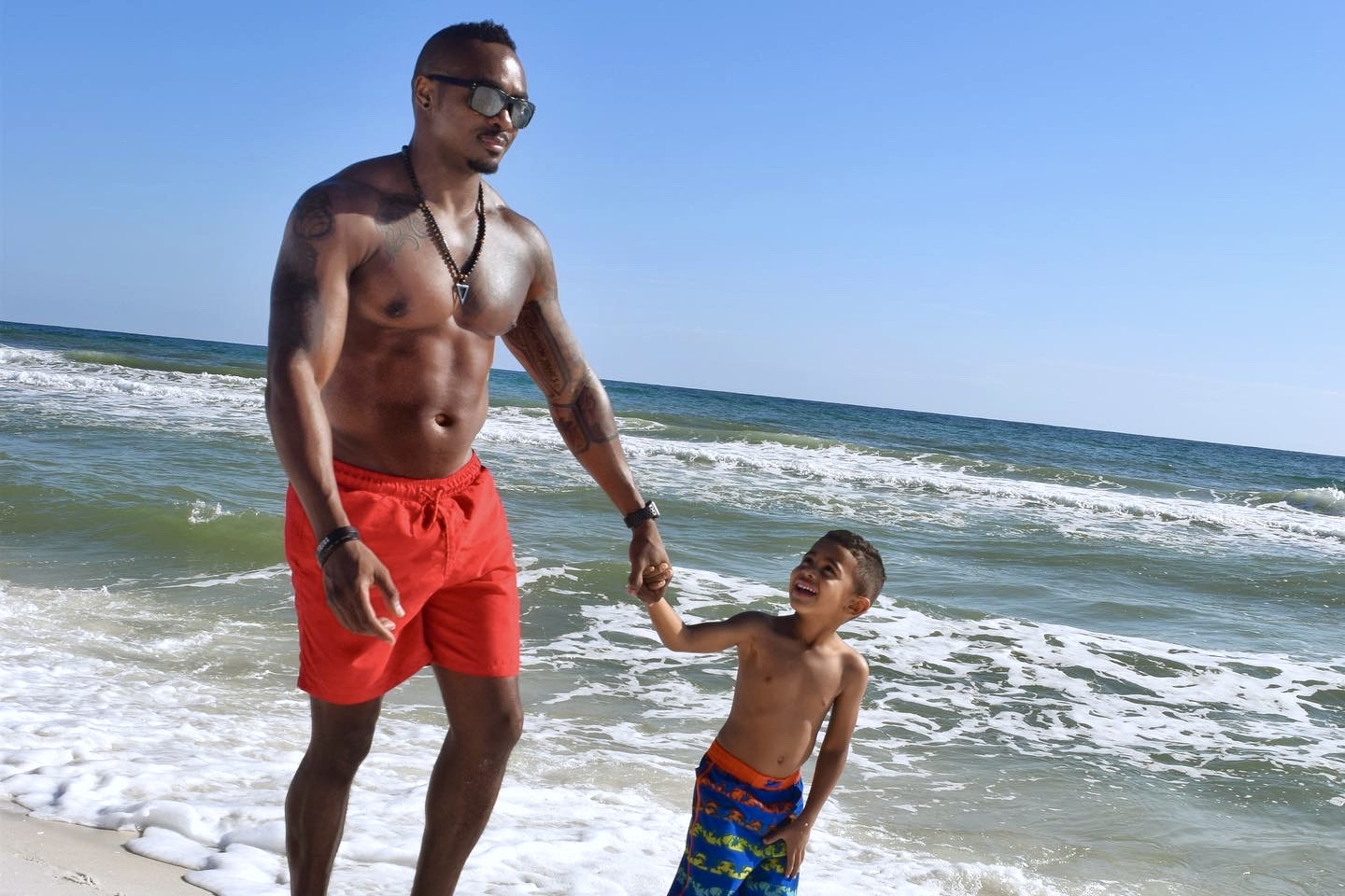 a father and his son on the beach, the little boy is looking up at his father smiling