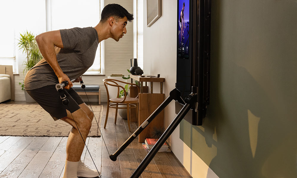 A man is working out in his living room. He is facing Tonal, completing a Barbell Bent Over Row.