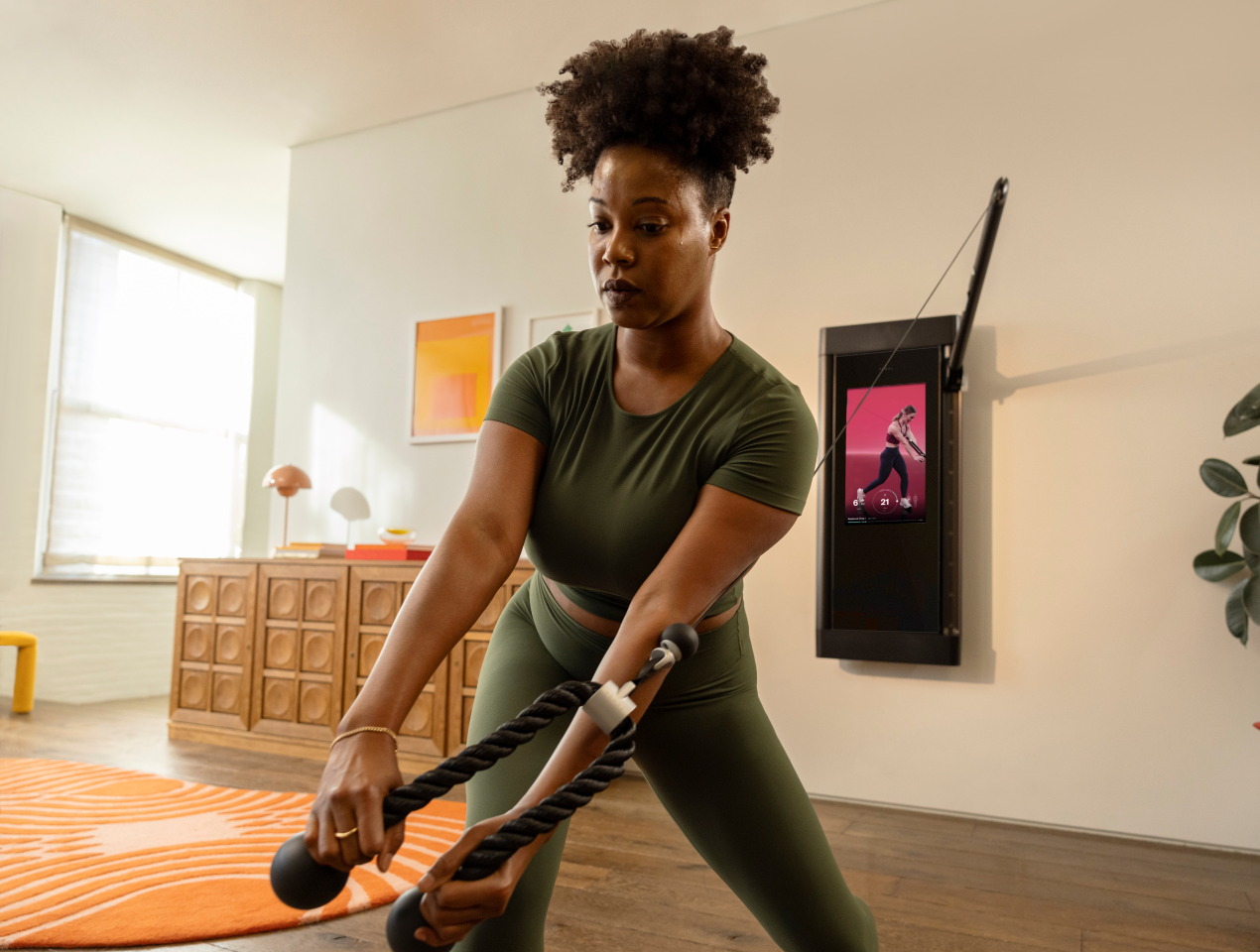 A woman is working out in her living room. She has her back to Tonal and is completing a Rotational Chop.