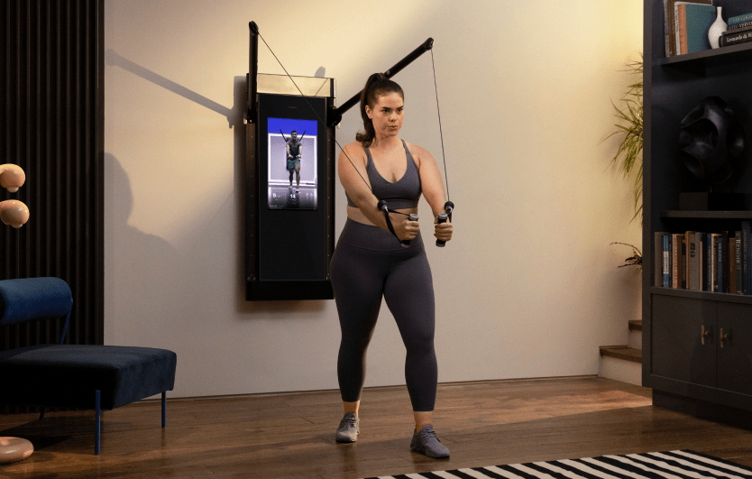 A woman is working out in her living room. She is facing away from Tonal, completing a Decline Chest Fly